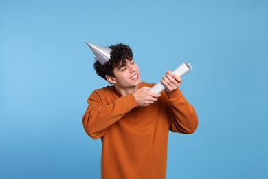 Photo of Handsome young man in party hat with popper on light blue background