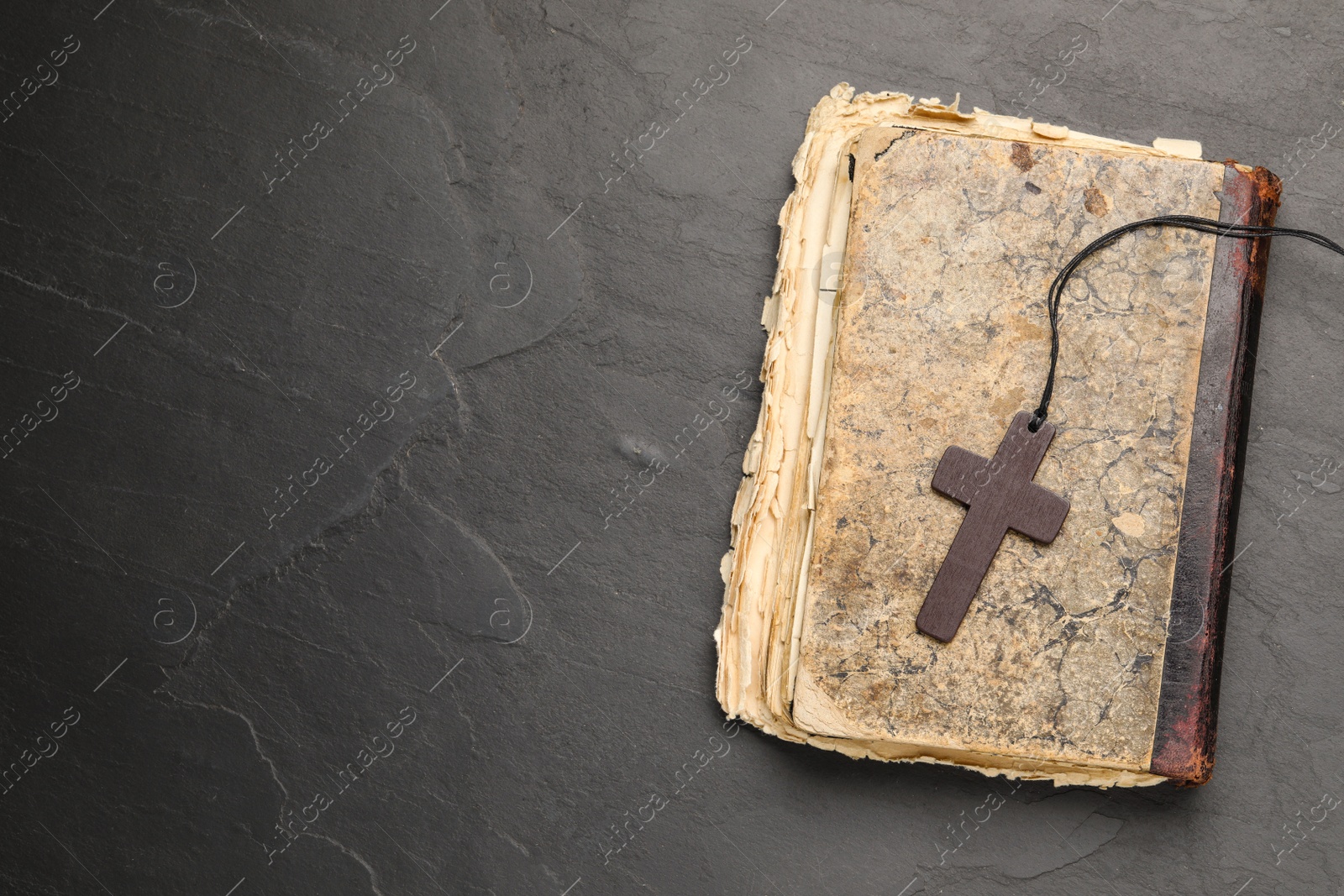 Photo of Wooden Christian cross and old Bible on black table, top view. Space for text