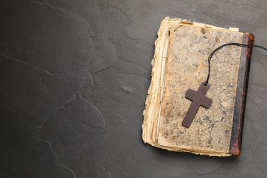 Photo of Wooden Christian cross and old Bible on black table, top view. Space for text