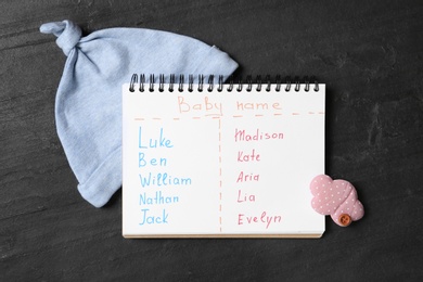 Photo of Notebook with written different baby names and child's accessories on black table, flat lay