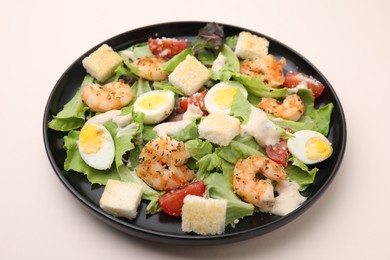 Delicious Caesar salad with shrimps on beige table, closeup