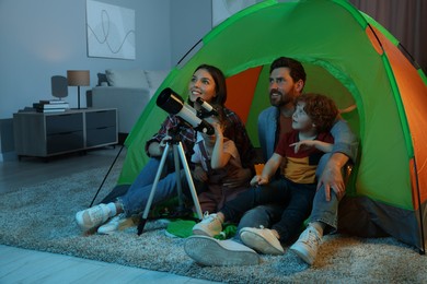 Photo of Happy family using telescope to look at stars while sitting in camping tent indoors