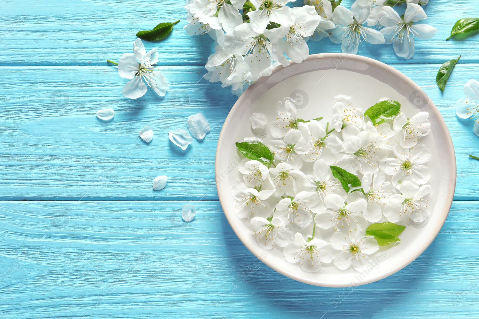 Photo of Bowl with water and blossoming flowers on wooden background