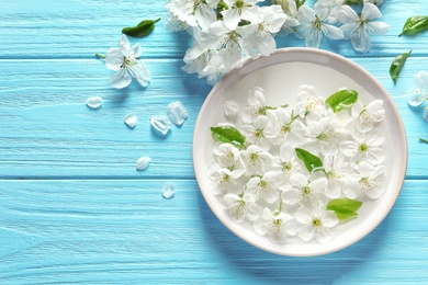 Photo of Bowl with water and blossoming flowers on wooden background