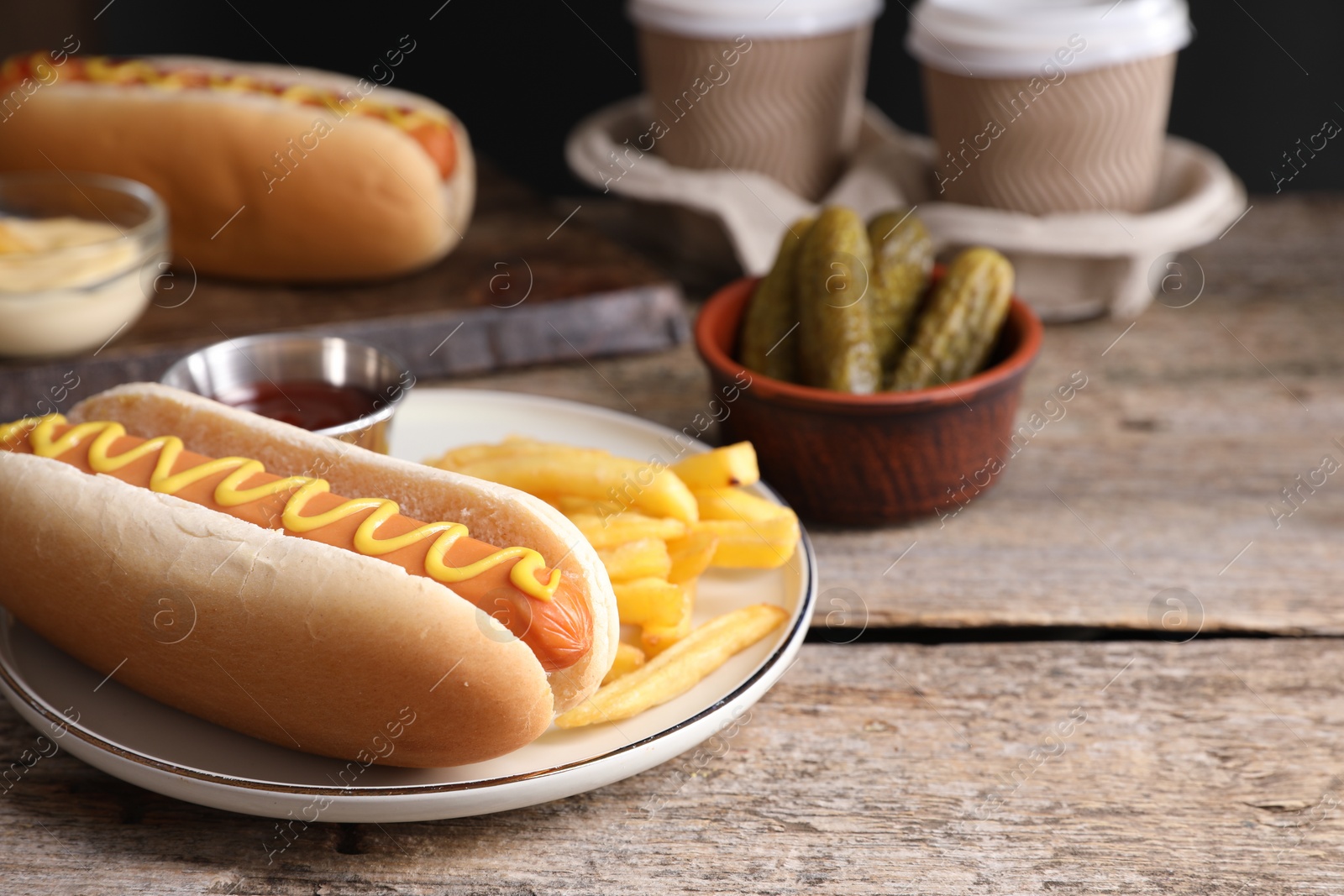 Photo of Delicious hot dog with mustard and French fries on wooden table, closeup. Space for text