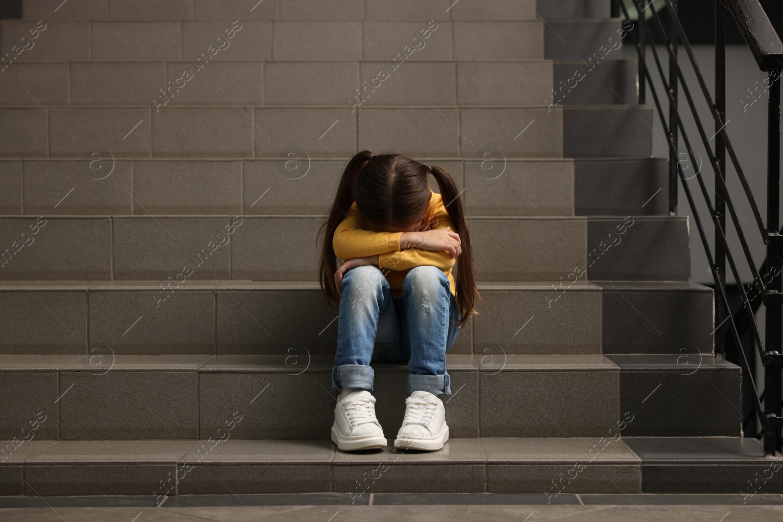 Photo of Child abuse. Upset little girl sitting on stairs indoors