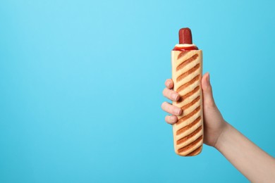 Photo of Woman holding delicious french hot dog on light blue background, closeup. Space for text