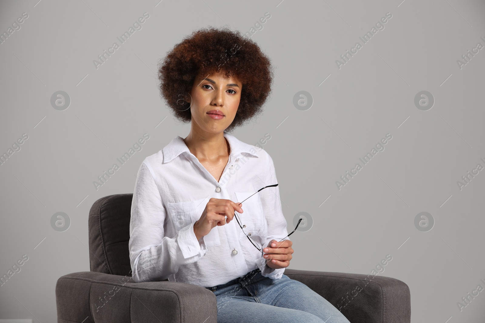 Photo of Beautiful young woman with eyeglasses sitting in armchair on grey background