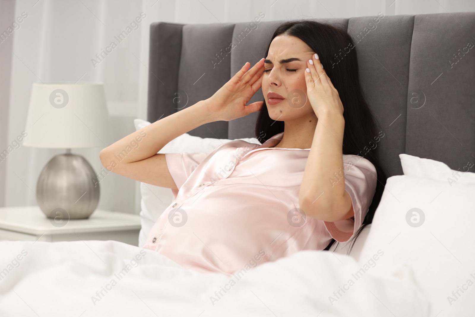 Photo of Pregnant woman suffering from headache in bed at home