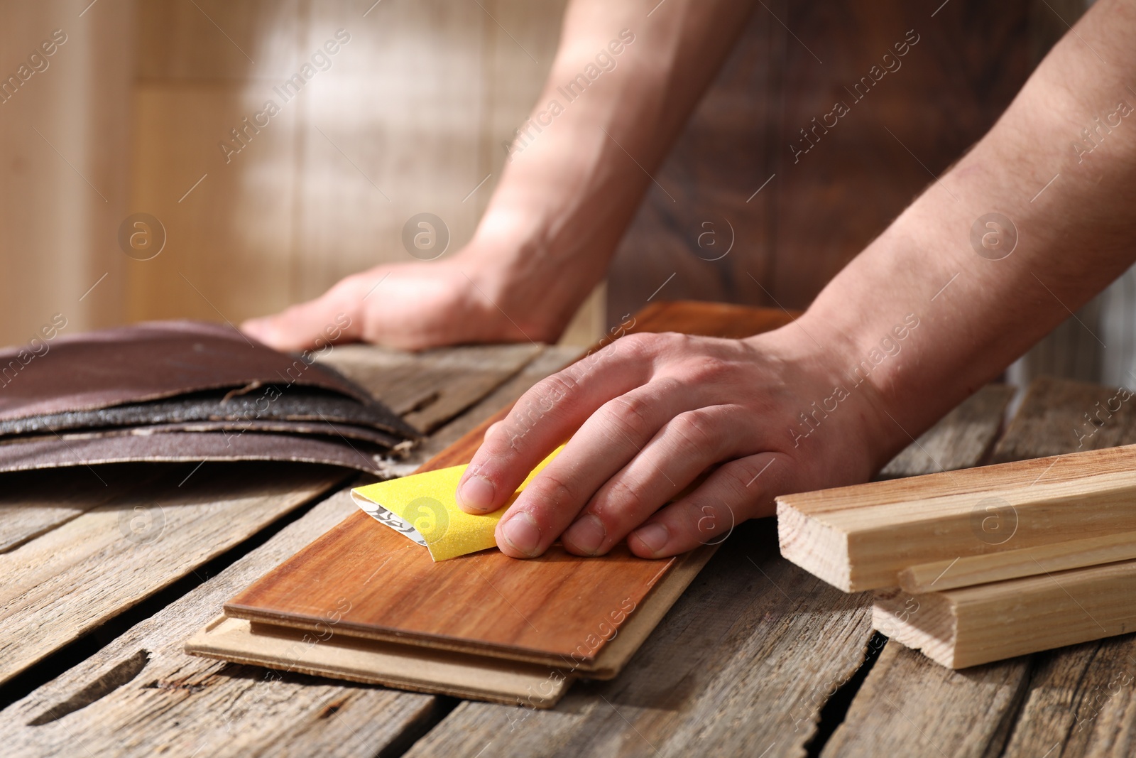 Photo of Man polishing wooden plank with sandpaper at table indoors, closeup