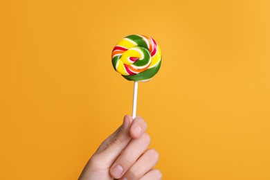 Woman holding bright tasty lollipop on orange background, closeup
