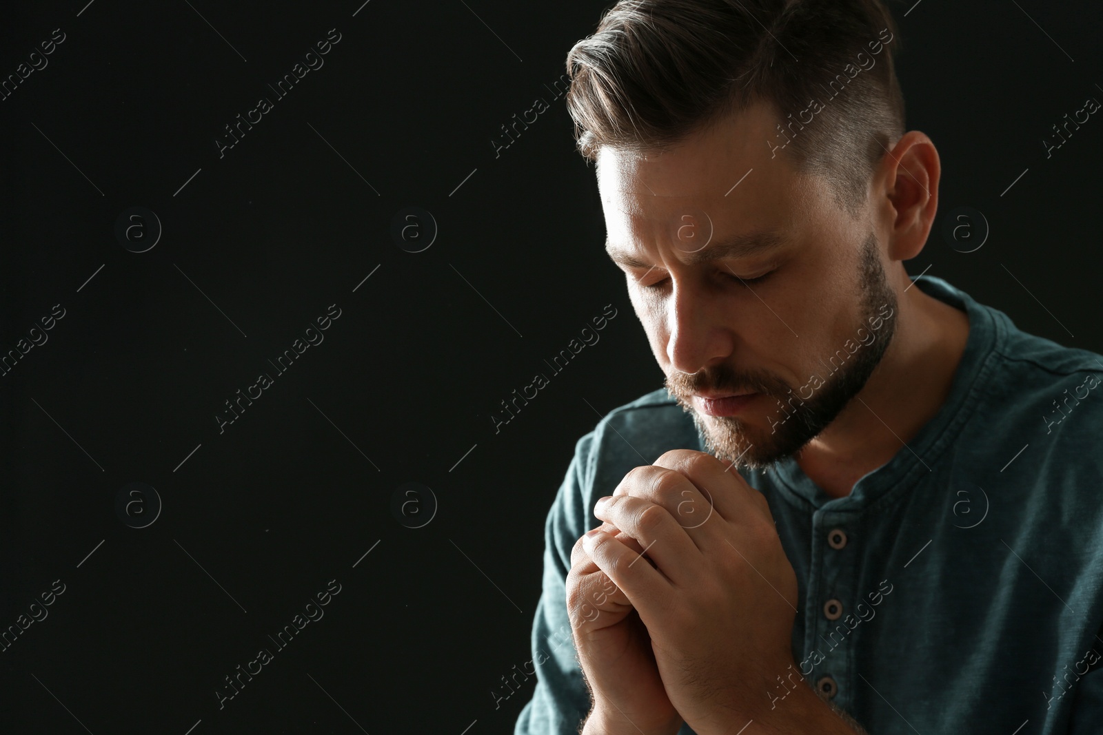 Photo of Man with hands clasped together for prayer on black background. Space for text