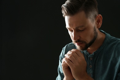 Photo of Man with hands clasped together for prayer on black background. Space for text