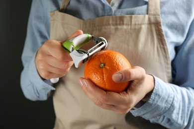 Woman peeling fresh orange on black background, closeup