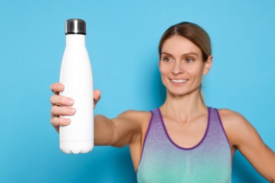 Sportswoman with thermo bottle on light blue background