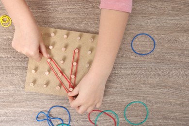 Photo of Motor skills development. Girl playing with geoboard and rubber bands at wooden table, top view