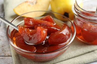 Photo of Taking tasty homemade quince jam from bowl at table, closeup