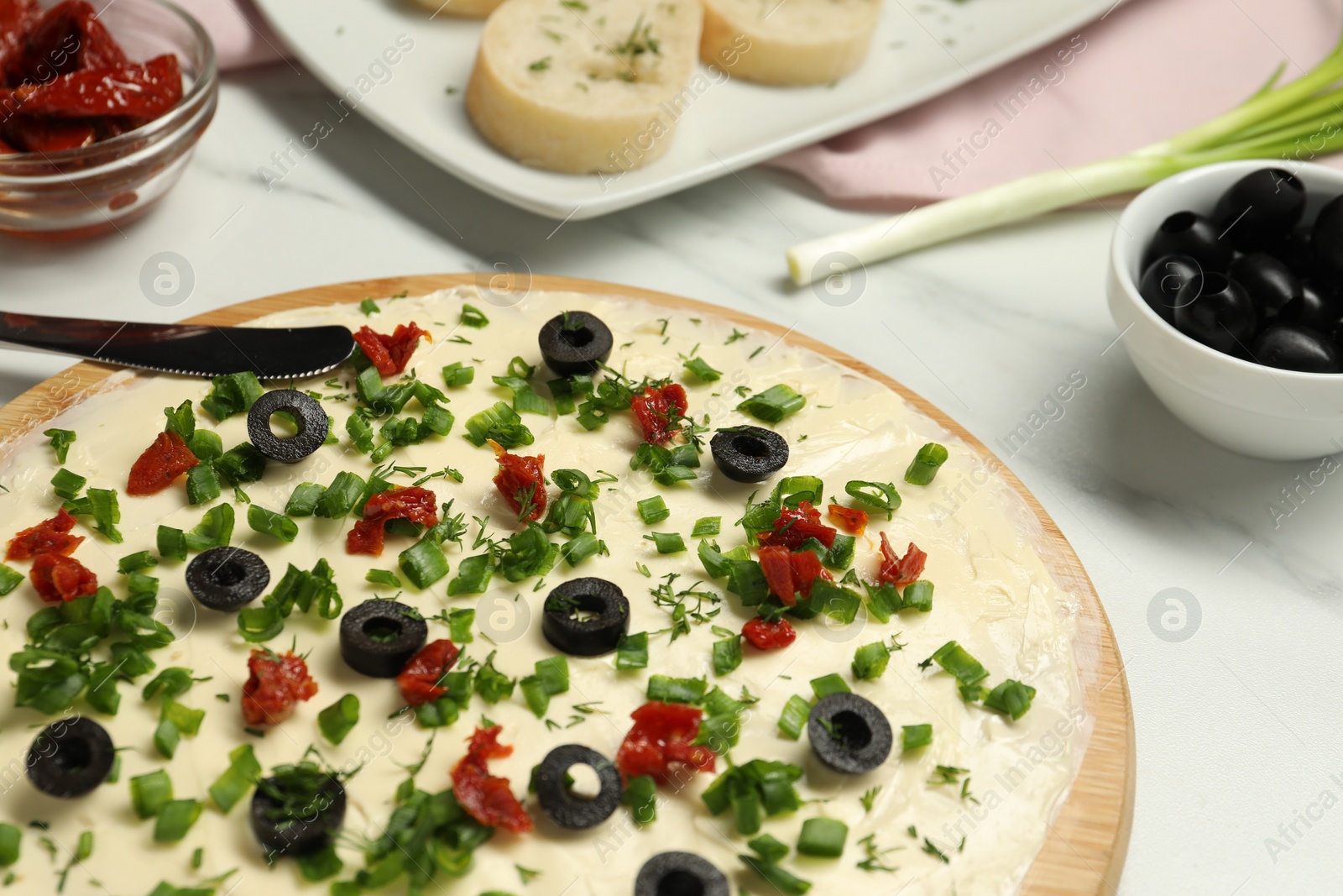 Photo of Fresh butter board with cut olives and onion on white table, closeup