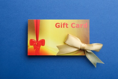 Photo of Gift card with bow on blue background, top view