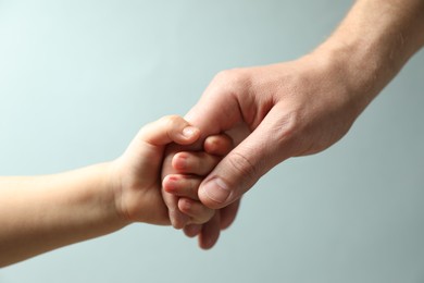 Photo of Father and child holding hands on light blue background, closeup