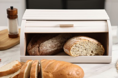 Photo of Wooden bread basket with freshly baked loaves on white marble table in kitchen