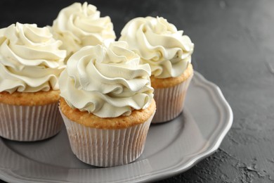 Photo of Tasty cupcakes with vanilla cream on black table, closeup