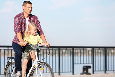 Photo of Father and daughter riding bicycle outdoors on sunny day