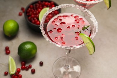 Tasty cranberry cocktail with rosemary and lime in glass on grey table, closeup