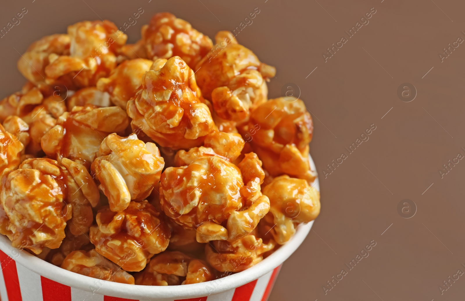 Photo of Delicious popcorn with caramel in paper bucket, closeup