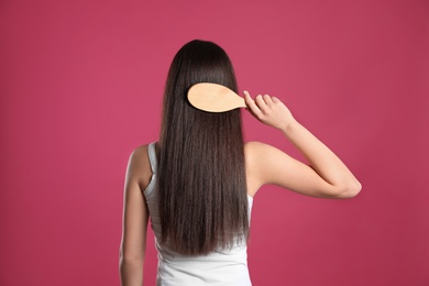 Back view of young woman with hair brush on color background