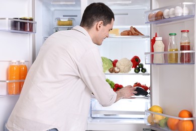 Photo of Happy man taking eggplant out of refrigerator in kitchen