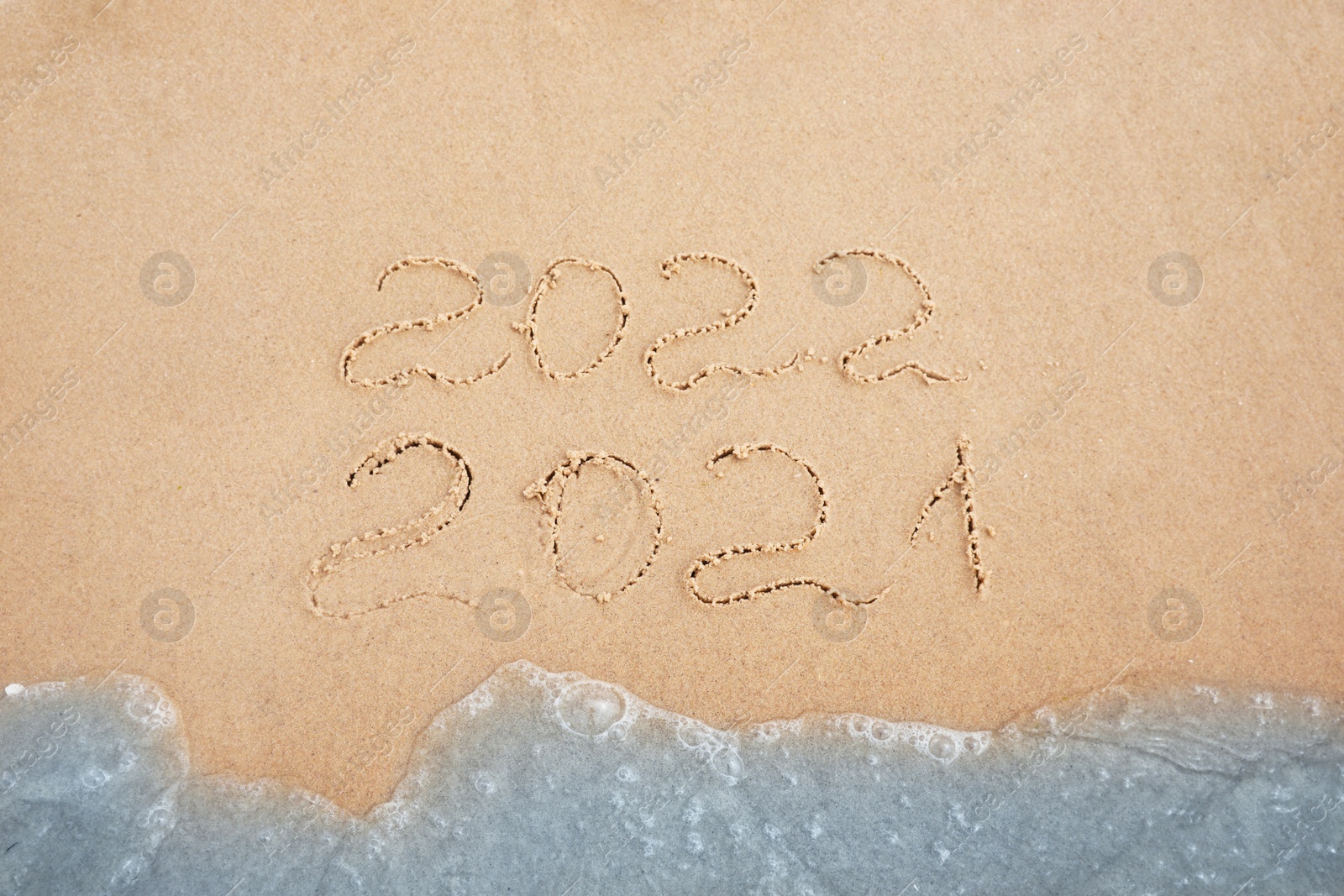 Photo of Dates written on sandy beach. 2021 washed by sea wave as New 2022 Year coming, above view