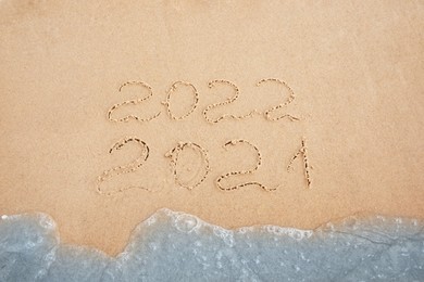 Dates written on sandy beach. 2021 washed by sea wave as New 2022 Year coming, above view