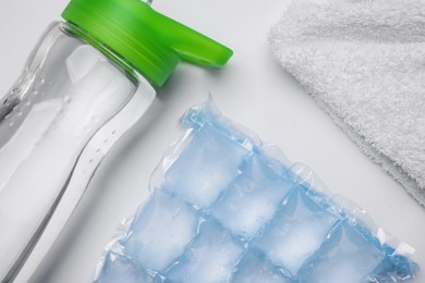 Bottle of water, ice pack and towel on white background, flat lay. Heat stroke treatment