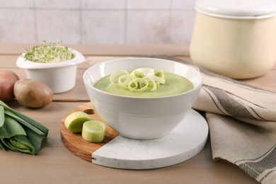 Photo of Tasty leek soup in bowl and fresh ingredients on wooden table