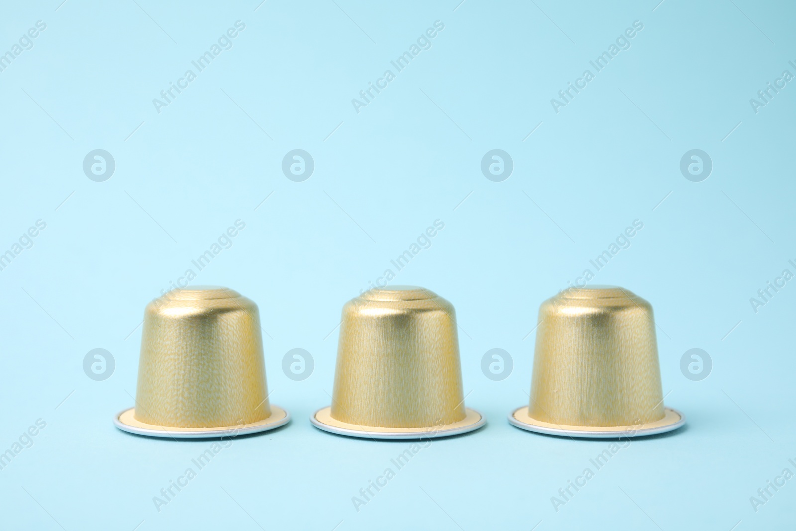 Photo of Three coffee capsules on light blue background, closeup