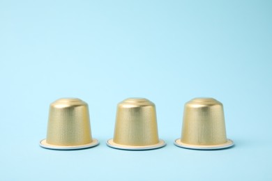 Three coffee capsules on light blue background, closeup