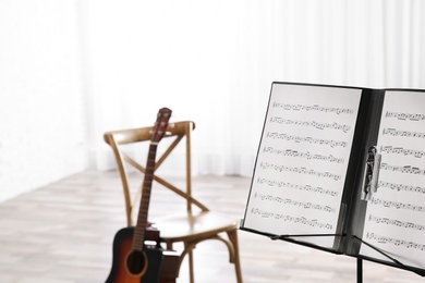 Photo of Note stand with music sheets and blurred acoustic guitar on background. Space for text