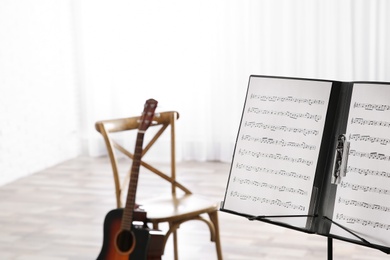 Note stand with music sheets and blurred acoustic guitar on background. Space for text