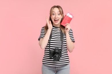 Excited young woman with passport, ticket and camera on pink background