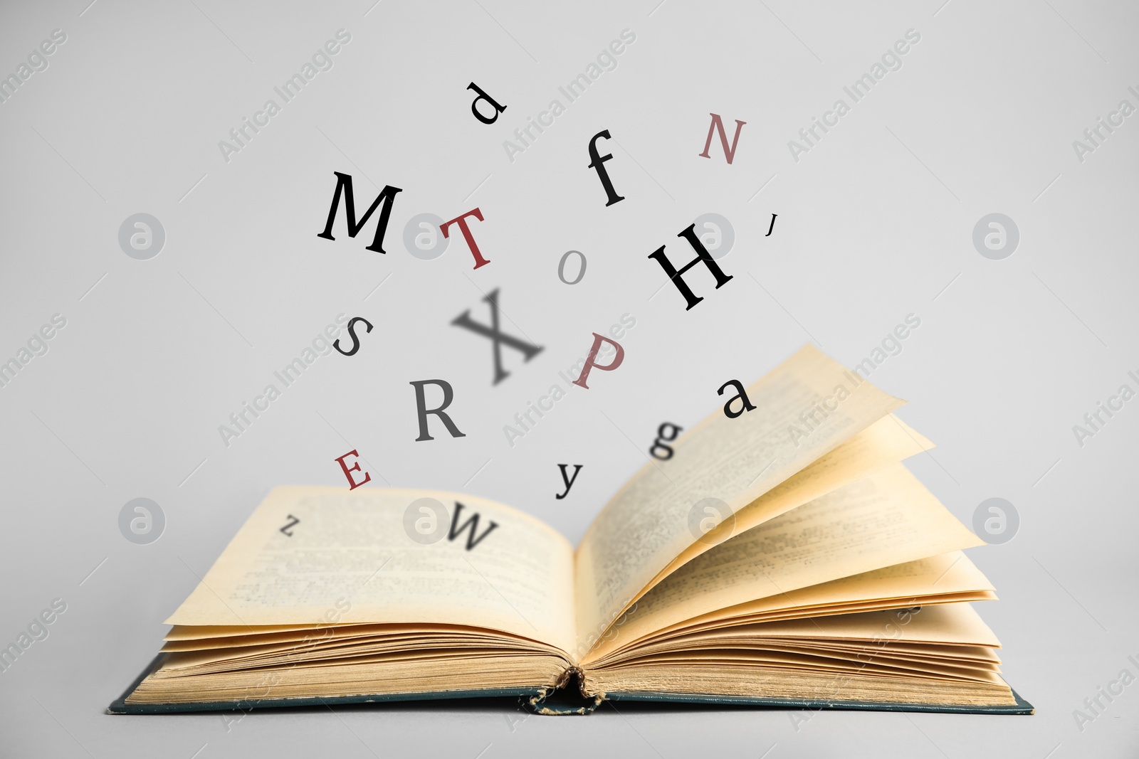 Image of Open book with letters flying out of it on light background