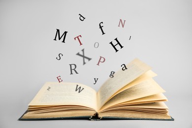 Image of Open book with letters flying out of it on light background