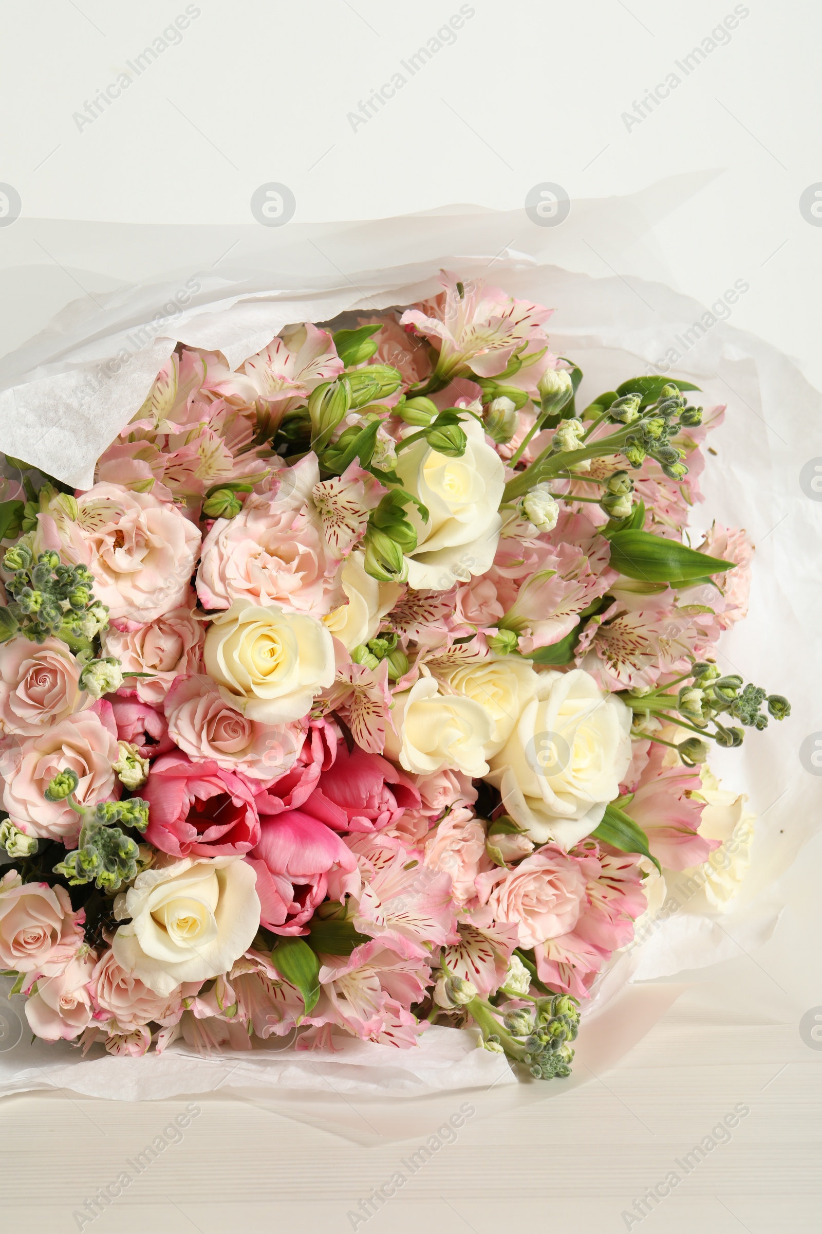 Photo of Beautiful bouquet of fresh flowers on wooden table near white wall