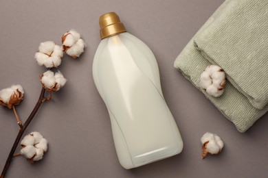 Photo of Bottle of fabric softener, terry towels and beautiful cotton flowers on gray background, flat lay