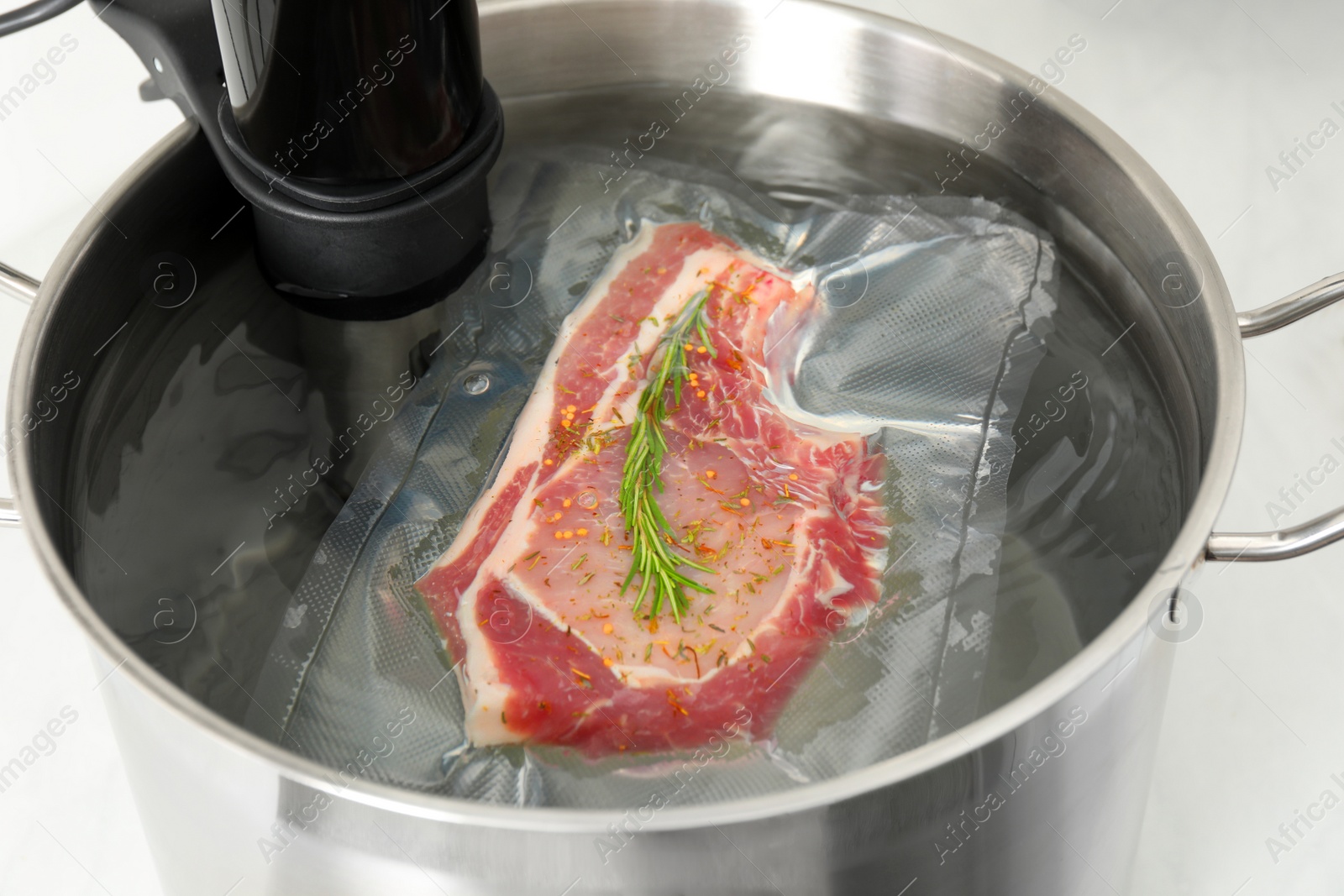 Photo of Sous vide cooker and vacuum packed meat in pot on table, closeup. Thermal immersion circulator