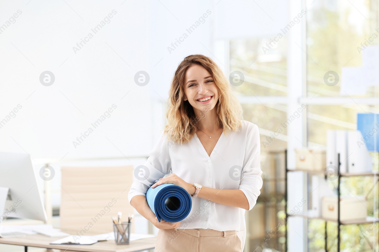 Photo of Young beautiful businesswoman holding yoga mat in office. Gym after work