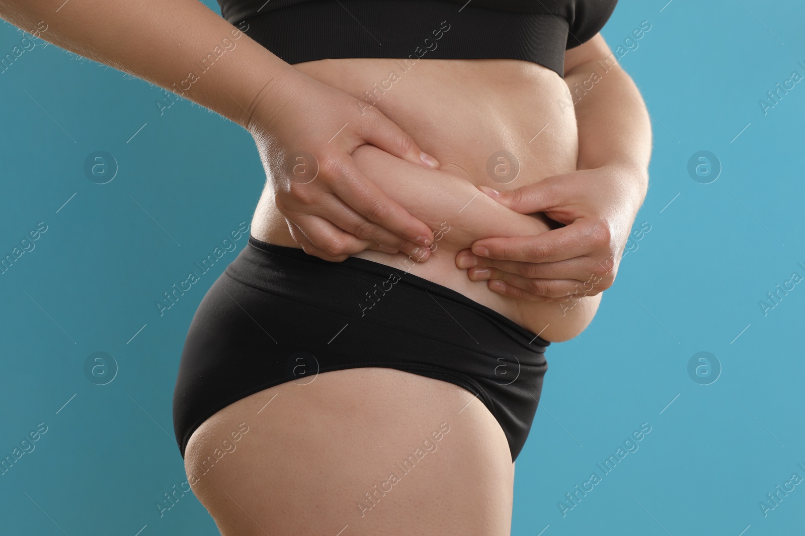 Photo of Woman touching belly fat on light blue background, closeup. Overweight problem