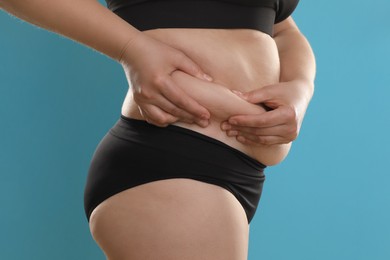 Woman touching belly fat on light blue background, closeup. Overweight problem