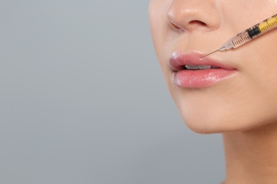 Young woman getting lips injection on grey background, space for text. Cosmetic surgery