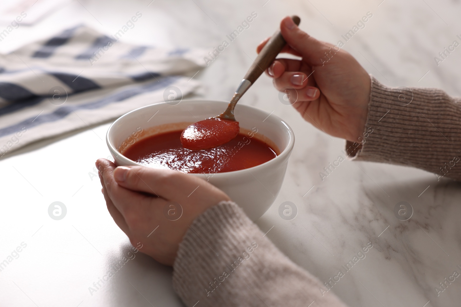 Photo of Woman eating tasty tomato soup at white marble table, closeup